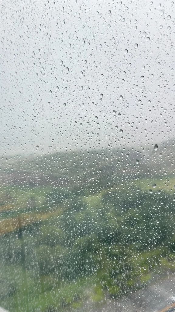Heavy raindrops on a window overlooking green scenery during Korea's summer monsoon season
