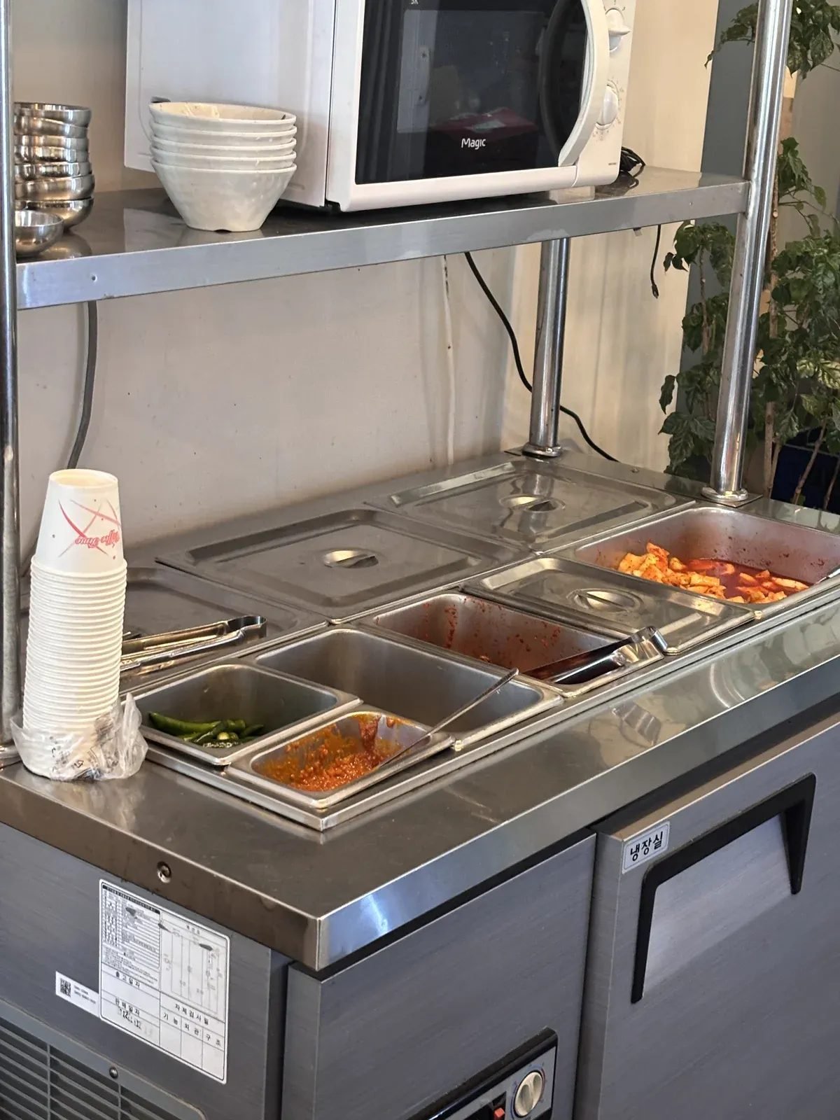 Stainless steel self-service side dish bar for free banchan refills at a Korean restaurant