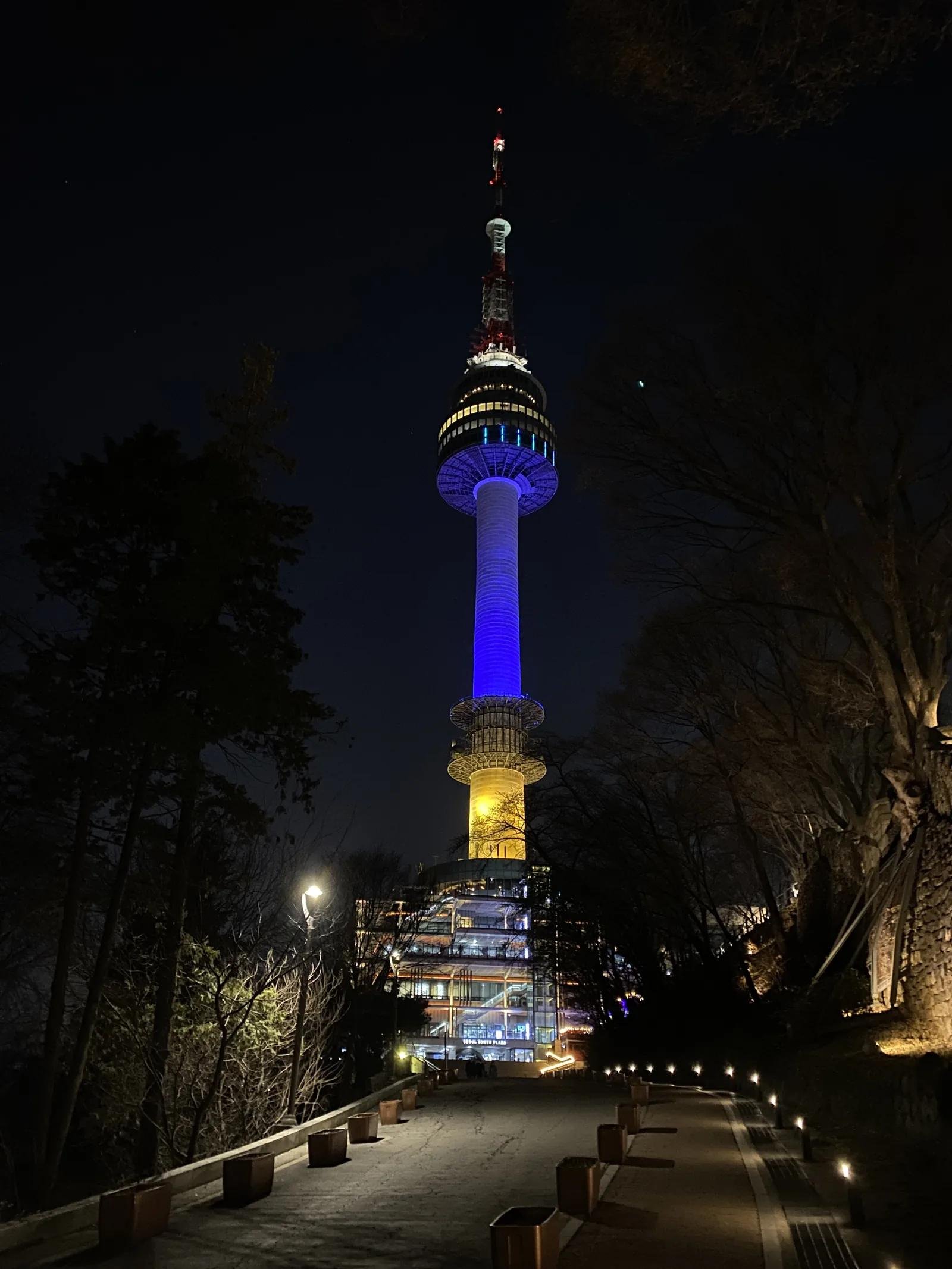 Illuminated N Seoul Tower at night glowing in blue over Namsan Mountain park