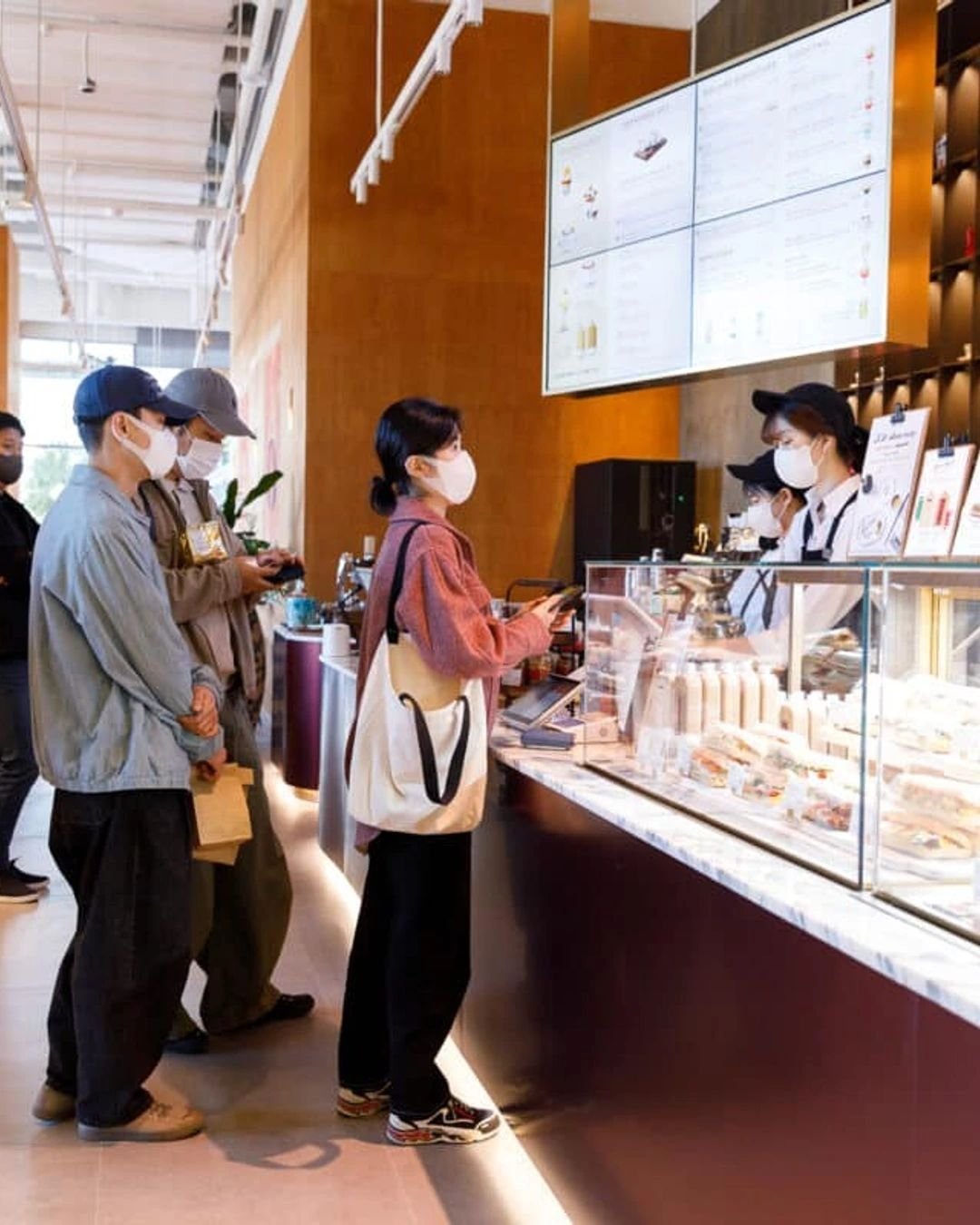 Travelers politely waiting in line to order and pay at a modern cafe counter in Seoul