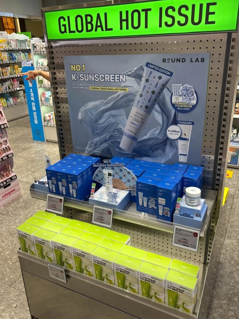 A 'Global Hot Issue' sunscreen display at an Olive Young store, featuring Round Lab's Birch Juice sunscreen.