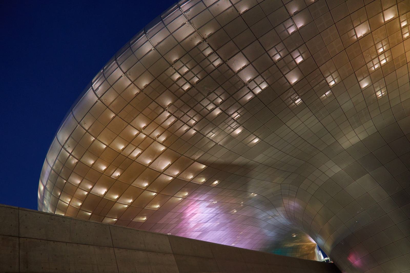 Curved exterior facade of Dongdaemun Design Plaza illuminated at night in Seoul.
