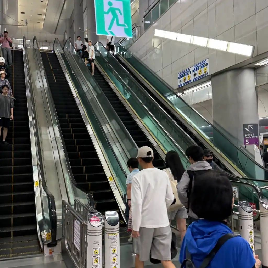 Travelers using escalators inside Gimpo Airport Station while transferring to Seoul subway lines