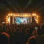 A large crowd watches an outdoor concert stage at night.