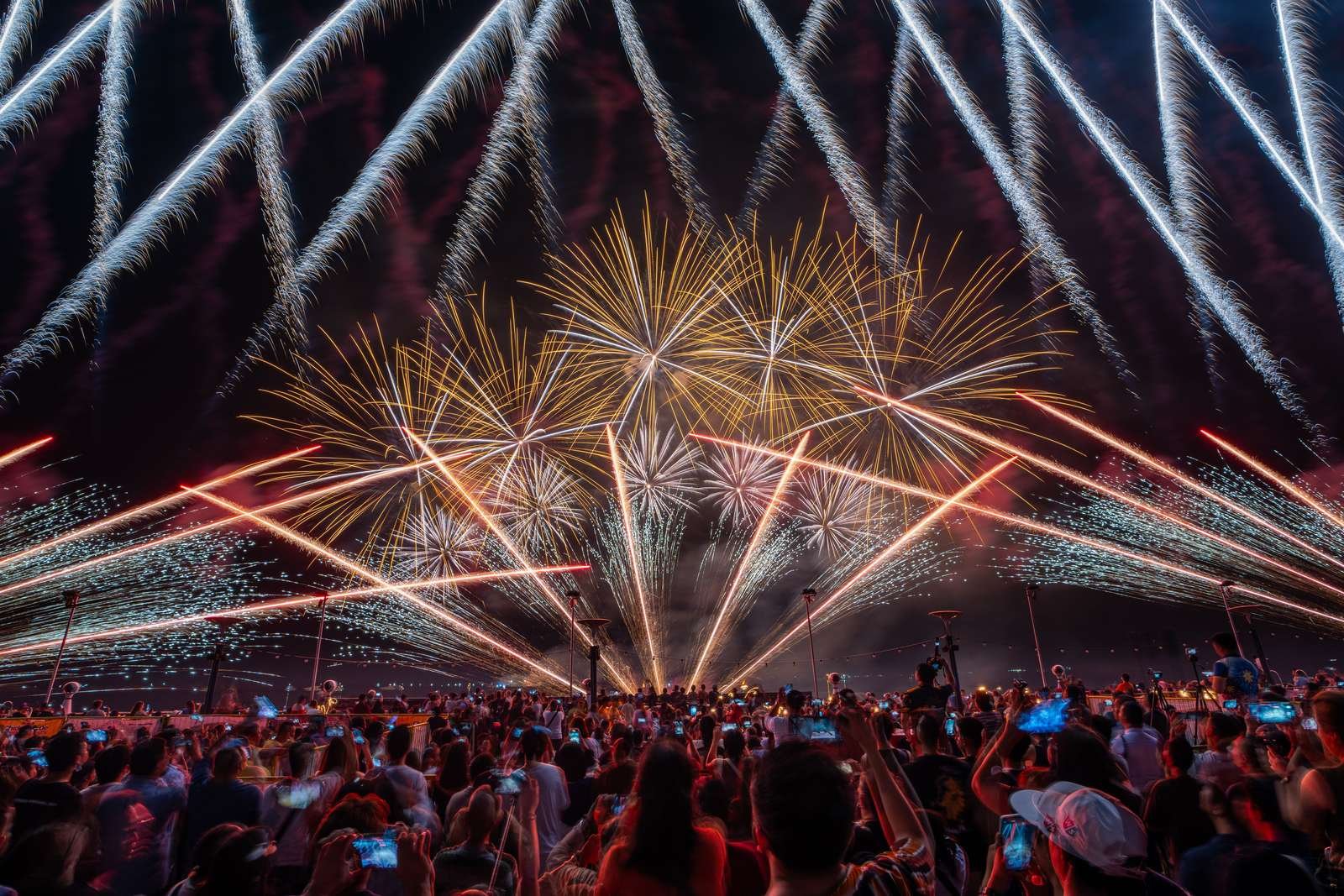 Fireworks burst above a large outdoor crowd at night.