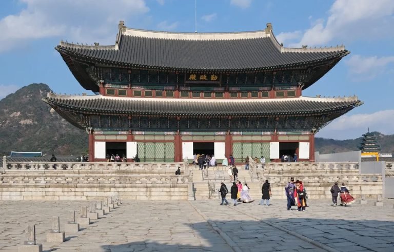 Visitors stand in the stone courtyard below Geunjeongjeon Hall at Gyeongbokgung Palace.
