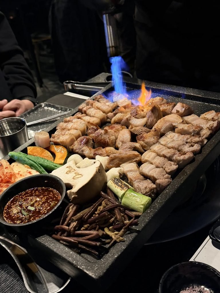 Samgyeopsal (pork belly) sizzling on a grill at a Korean BBQ restaurant.