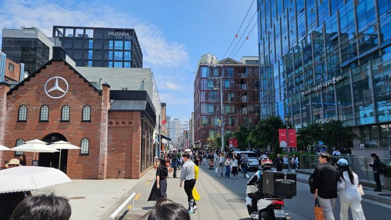 Pedestrians on a sunny Seongsu street lined with red-brick and glass-fronted buildings.