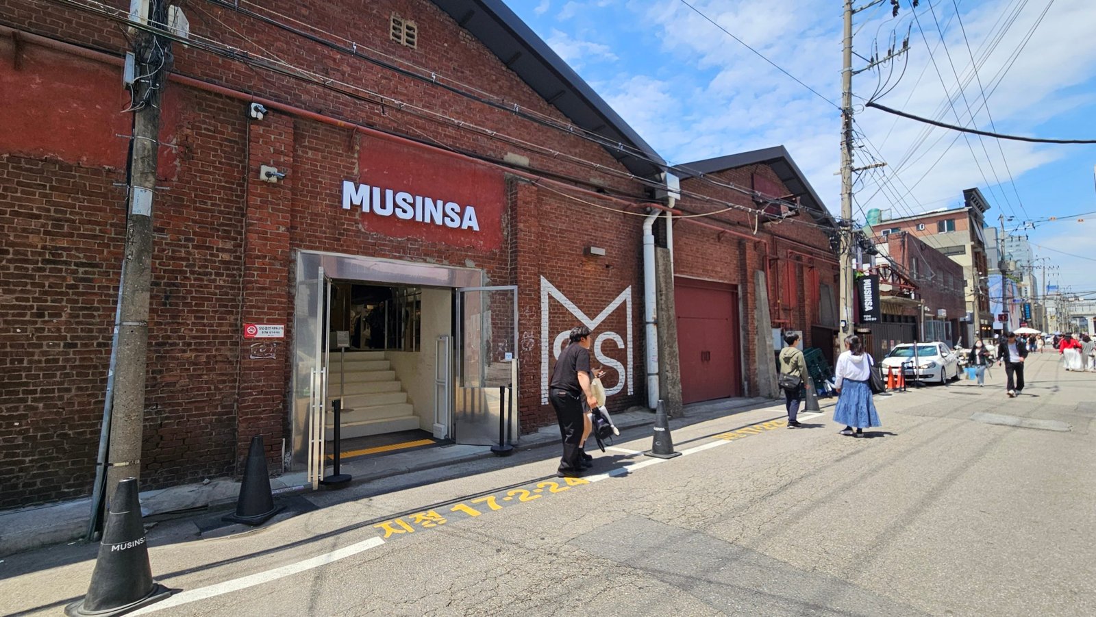 Red-brick MUSINSA storefront with pedestrians walking along the street in Seongsu.