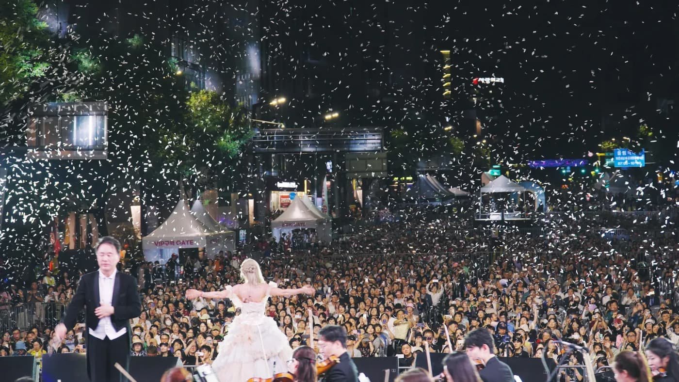 A conductor and orchestra perform for a large nighttime crowd at the 2025 Seoripul Music Festival classical concert.
