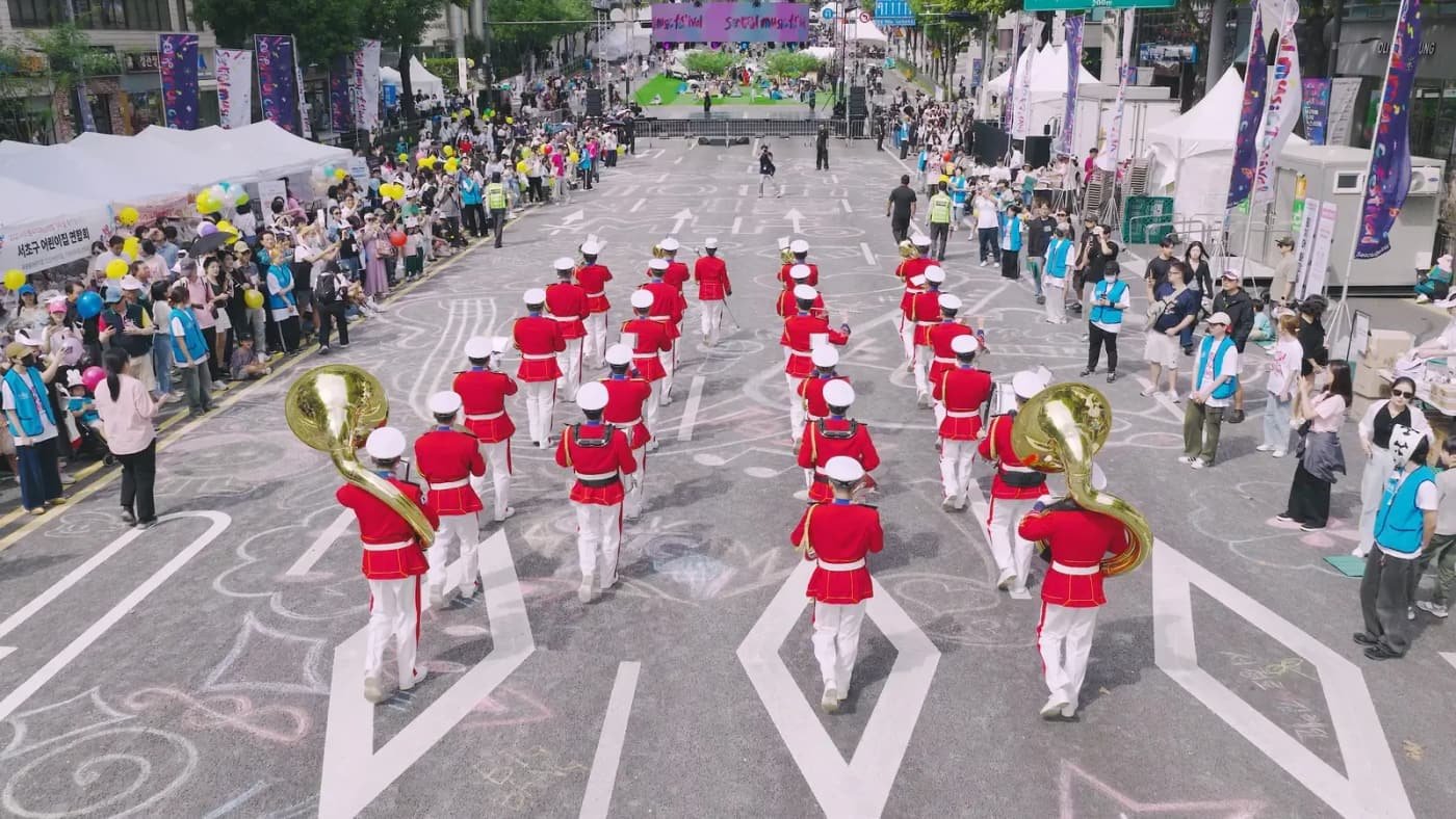 A marching band in red uniforms performs down Banpo-daero as spectators watch the 2025 Seoripul Music Festival opening parade.