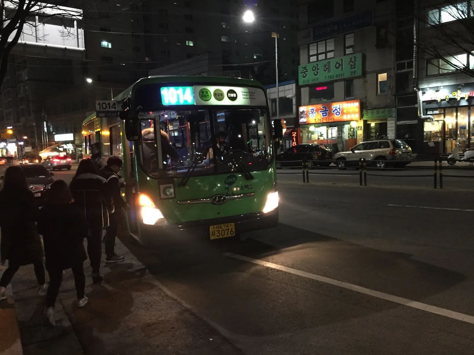 A green Seoul city bus numbered 1014 stops beside passengers on a lit street at night.