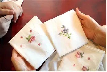 Hands hold pale embroidered fabric decorated with small colorful flowers at the 2024 heritage festival.