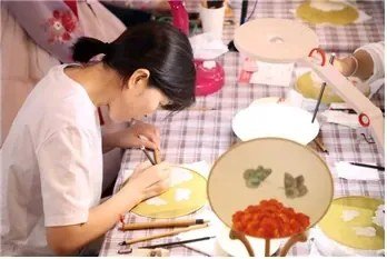 A participant paints flowers on a round fan during a folk-painting activity at the 2024 festival.