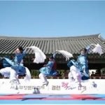 Taekkyeon performers leap on an outdoor stage in front of tiled hanok roofs at the 2024 Seoul heritage festival.