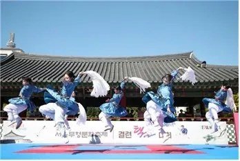 Taekkyeon performers leap on an outdoor stage in front of tiled hanok roofs at the 2024 Seoul heritage festival.