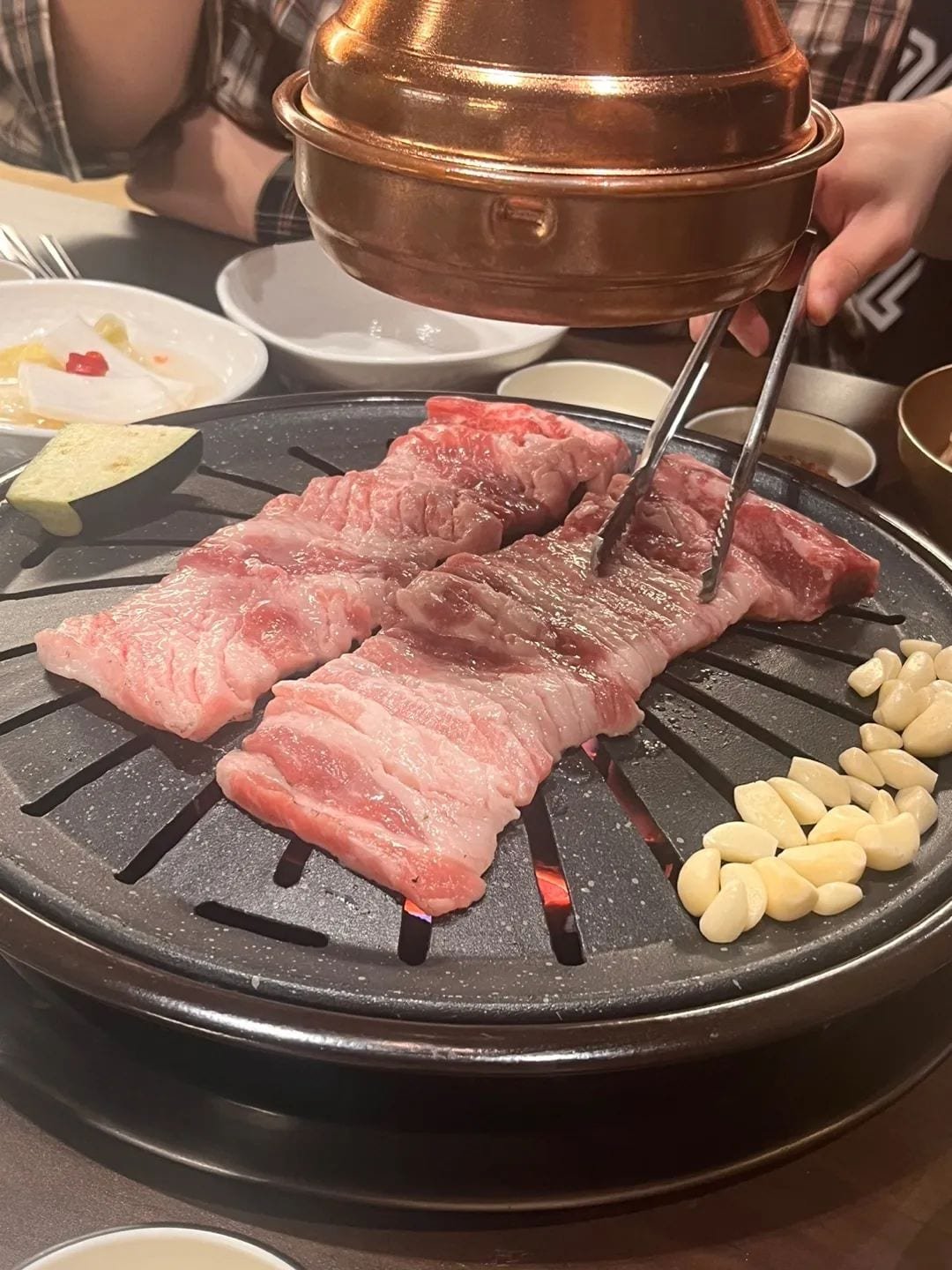 Thick-cut pork grilling at a Korean barbecue restaurant table.