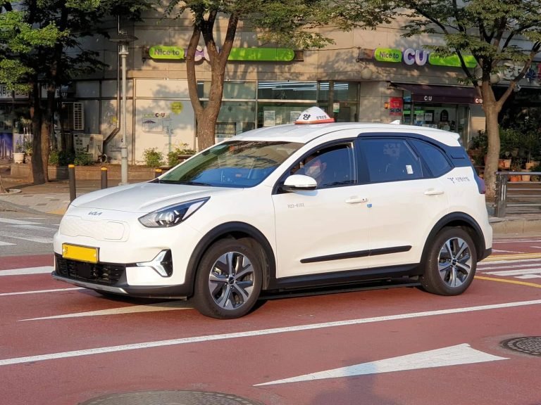 White Kia Niro Plus electric taxi on a street in Seoul.